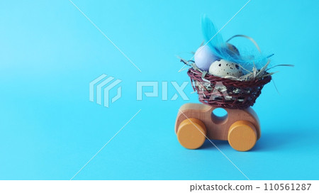On a wooden toy car Easter basket with quail eggs, hay and feathers, on a blue background On a wooden toy car Easter basket with quail eggs, hay and feathers, on a blue background 110561287