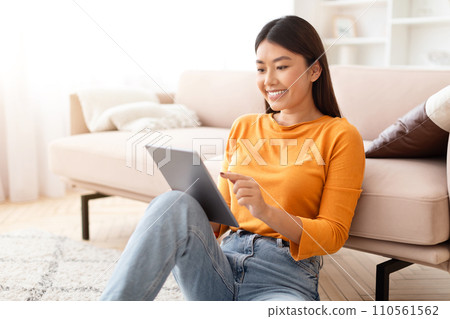 Happy asian woman reading news on digital tablet, home interior Happy asian woman reading news on digital tablet, home interior 110561562