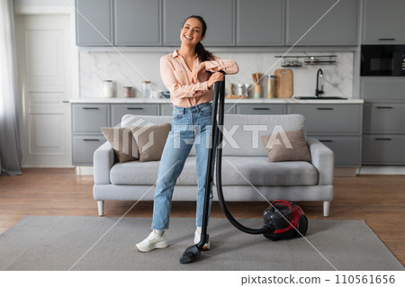 Joyful woman with vacuum in a chic, modern living area Joyful woman with vacuum in a chic, modern living area 110561656