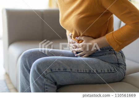 Unrecognizable woman experiencing abdominal pain at home, touching her stomach 110561669