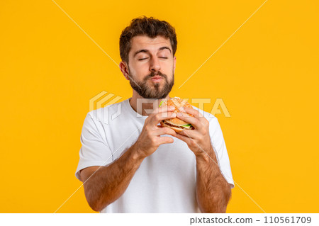 Hungry European Young Man Eating Tasty Burger Against Yellow Backdrop 110561709