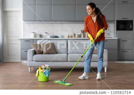 Smiling woman mopping floor with a bucket of supplies nearby Smiling woman mopping floor with a bucket of supplies nearby 110561714