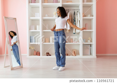 Happy black woman in oversized jeans looking in the mirror Happy black woman in oversized jeans looking in the mirror 110561721