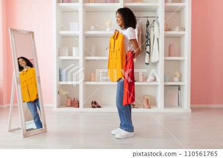 Woman choosing between yellow and red tops, mirror view Woman choosing between yellow and red tops, mirror view 110561765