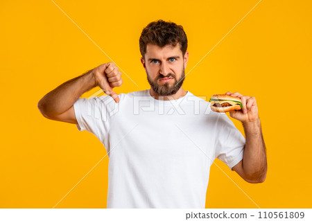 Man Holding Burger Gesturing Thumb Down Disapproving Unhealthy Nutrition, Studio 110561809