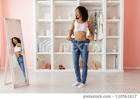 Smiling black woman in loose jeans celebrates weight loss Smiling black woman in loose jeans celebrates weight loss 110561817