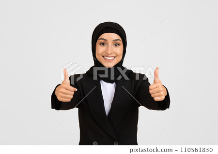 Happy muslim european businesswoman giving thumbs-up with both hands, dressed in black suit and hijab Happy muslim european businesswoman giving thumbs-up with both hands, dressed in black suit and hijab 110561830