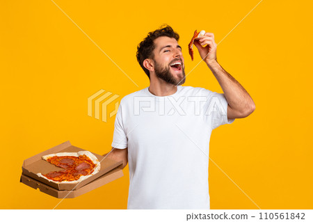 Man Eating Pizza Holding Pizzeria Box Over Yellow Studio Backdrop 110561842