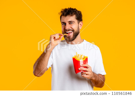 Young Guy Eating French Fries Over Yellow Studio Backdrop 110561846