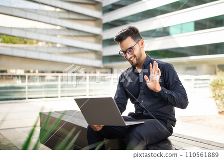 Professional businessman waves hello during video call on laptop outside 110561889