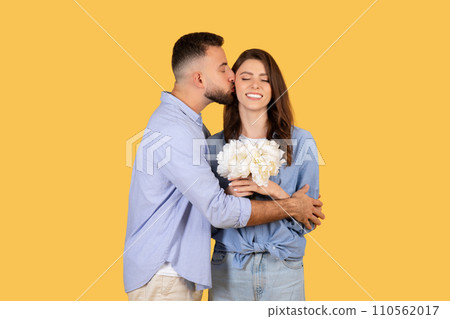 Man kissing woman on cheek, she holds flowers, expressing affection 110562017
