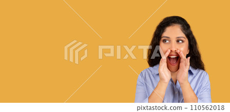 Excited young woman with curly hair shouting an announcement with hands cupped around her mouth 110562018