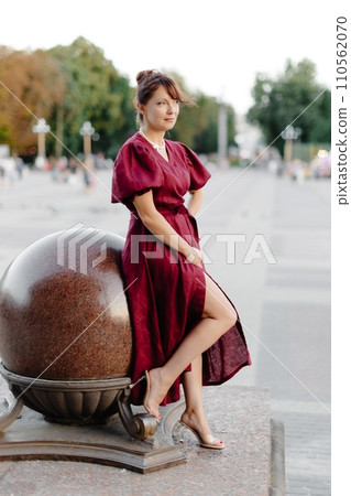 Attractive girl with hairstyle, in red dress is standing on street on old building background Attractive girl with hairstyle, in red dress is standing on street on old building background 110562070