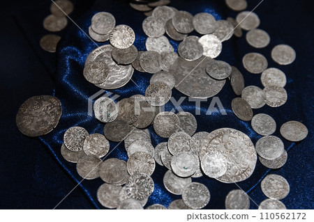 Ancient silver coins lay on deep blue silk, close up Ancient silver coins lay on deep blue silk, close up 110562172