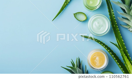 Natural aloe skincare flat lay, glass containers with gel and creams, surrounded by aloe vera leaves. Blue background 110562761