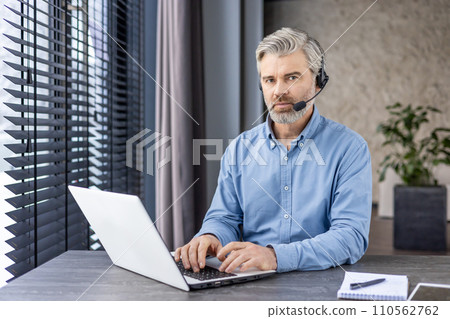 Professional middle-aged man with headset working on laptop in a modern office setting, showcasing focus and efficiency. 110562762