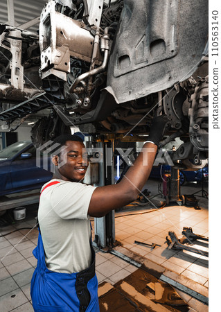 Young African mechanic in uniform working under the car in car service center 110563140