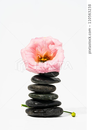 Stacked black spa stones with flowers on white background Stacked black spa stones with flowers on white background 110563238