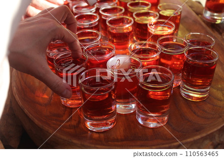 Red alcohol tincture in small glasses is dismantled by people. Alcoholic homemade beverages 110563465