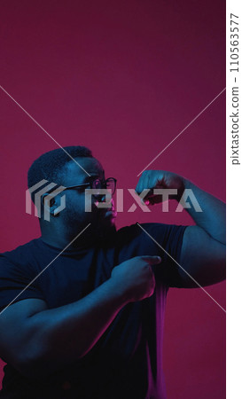 Showing power. Color light people. Strong confident man in glasses pointing at his biceps isolated on dark pink empty space background. 110563577