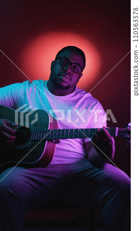 Guitar music. Artist playing. Talented concentrated man performing song chords on string instrument on isolated on neon light dark background. 110563578