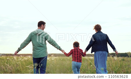 Parents and son energetically run holding each other hands across open field Parents and son energetically run holding each other hands across open field 110563628