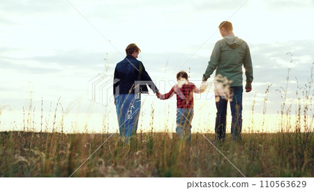 Happy family enjoys walk in field embracing joyous moments brought by wind Happy family enjoys walk in field embracing joyous moments brought by wind 110563629