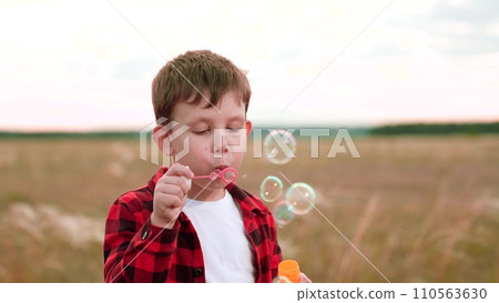 Happy boy finds happiness in blowing bubbles in field of cultivated plants Happy boy finds happiness in blowing bubbles in field of cultivated plants 110563630