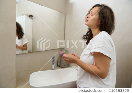 Worried young woman reflected in home mirror, concerned about hair loss, combing at mirror, holding hair brush and lock. Worried young woman reflected in home mirror, concerned about hair loss, combing at mirror, holding hair brush and lock. 110563899