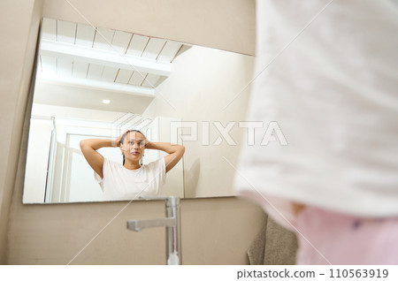 Beautiful woman looking at her mirror reflection while applying cosmetics on her face with radiant clean healthy skin 110563919