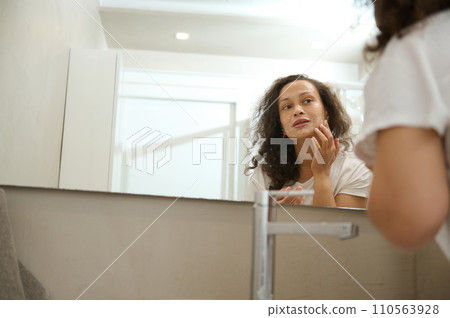 Young pretty woman looks at the mirror while applies moisturizing cleansing foam on face during morning spa procedures Young pretty woman looks at the mirror while applies moisturizing cleansing foam on face during morning spa procedures 110563928