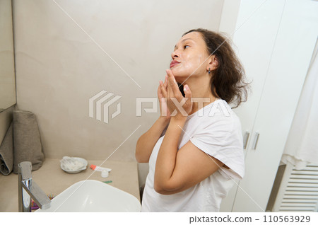 Young beautiful woman applying cleansing foam on her face during morning beauty procedures in the home bathroom 110563929