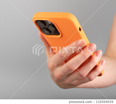 Berlin Germany December 21 2023 Hand holding iphone in bright orange silicone case Berlin Germany December 21 2023 Hand holding iphone in bright orange silicone case 110564039