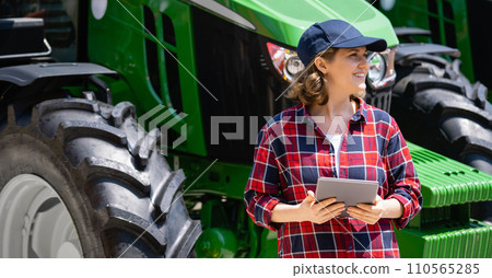 Woman farmer with a digital tablet on the background of an agricultural tractor. Woman farmer with a digital tablet on the background of an agricultural tractor. 110565285