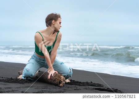 Woman striking playful pose on log, sitting like riding horse, turning head to side with eyes closed Woman striking playful pose on log, sitting like riding horse, turning head to side with eyes closed 110567821