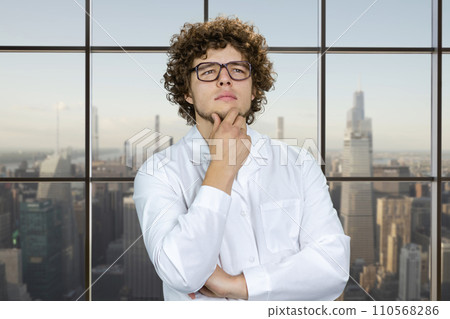 Portrait of a smart thoughtful young man with curly hair. Checkered window with cityscape view in the background. Portrait of a smart thoughtful young man with curly hair. Checkered window with cityscape view in the background. 110568286