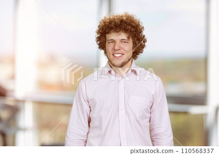 Portrait of a happy young cheerful man with curly hair. Indoor window in the background. Portrait of a happy young cheerful man with curly hair. Indoor window in the background. 110568337