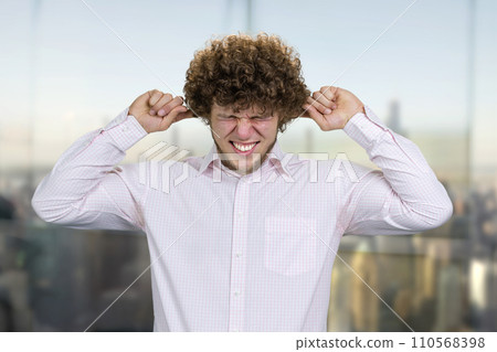 Caucasian young man in white shirt close his ears with both fingers. He doesn't want to hear that. Nervous breakdown concept. Blurred cityscape in the background. Caucasian young man in white shirt close his ears with both fingers. He doesn't want to hear that. Nervous breakdown concept. Blurred cityscape in the background. 110568398