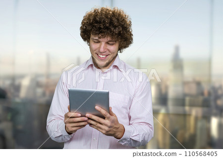 Excited young happy caucasian man holding a tablet pc device. Guy playing mobile videogame app or watching digital video stream holding cell phone indoors. Excited young happy caucasian man holding a tablet pc device. Guy playing mobile videogame app or watching digital video stream holding cell phone indoors. 110568405