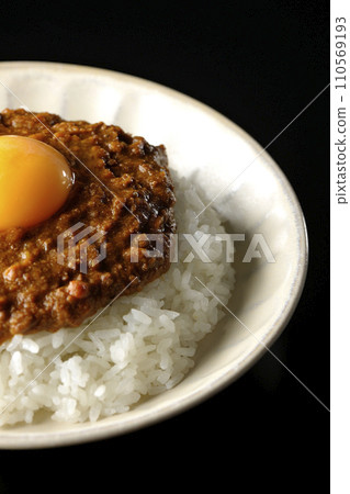 Keema curry topped with egg yolk photographed against a black background 110569193