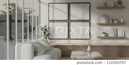 A modern white-furnished living room designed with a white cosy couch and blank frames on the wall. 110569797