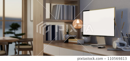 A PC computer and accessories on a table, a wooden bookshelf, and decor in a modern office room. 110569813