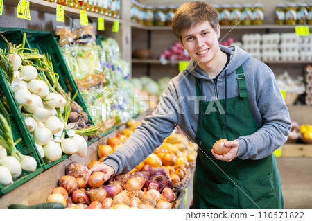 Male seller working in supermarket and lays out onions on counter 110571822