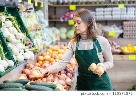 Female seller working in supermarket and lays out onions on counter Female seller working in supermarket and lays out onions on counter 110571875