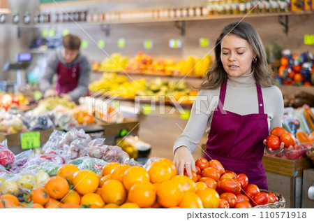 Young female seller holding tomatoes standing by counter in grocery market Young female seller holding tomatoes standing by counter in grocery market 110571918