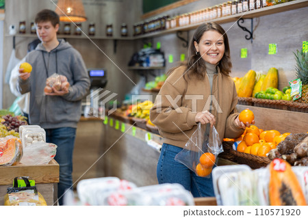 Young woman selects and buys fresh oranges in grocery store 110571920