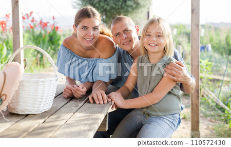 Family of three sitting at table outdoors 110572430