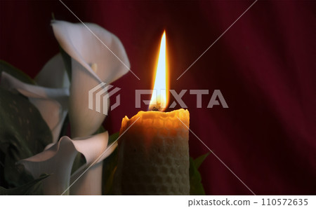 Candle flame and white lily in surrounding darkness Candle flame and white lily in surrounding darkness 110572635