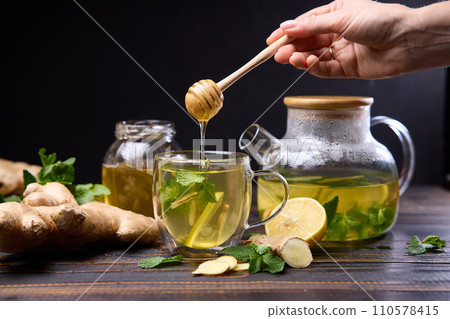 woman pours honey in a cup with natural organic herbal tea and glass teapot on a wooden table 110578415