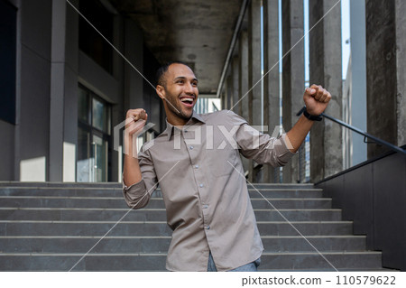 Joyful young man celebrating success with a fist pump gesture on urban stairs. Euphoria, achievement, and happiness in a casual setting. Joyful young man celebrating success with a fist pump gesture on urban stairs. Euphoria, achievement, and happiness in a casual setting. 110579622